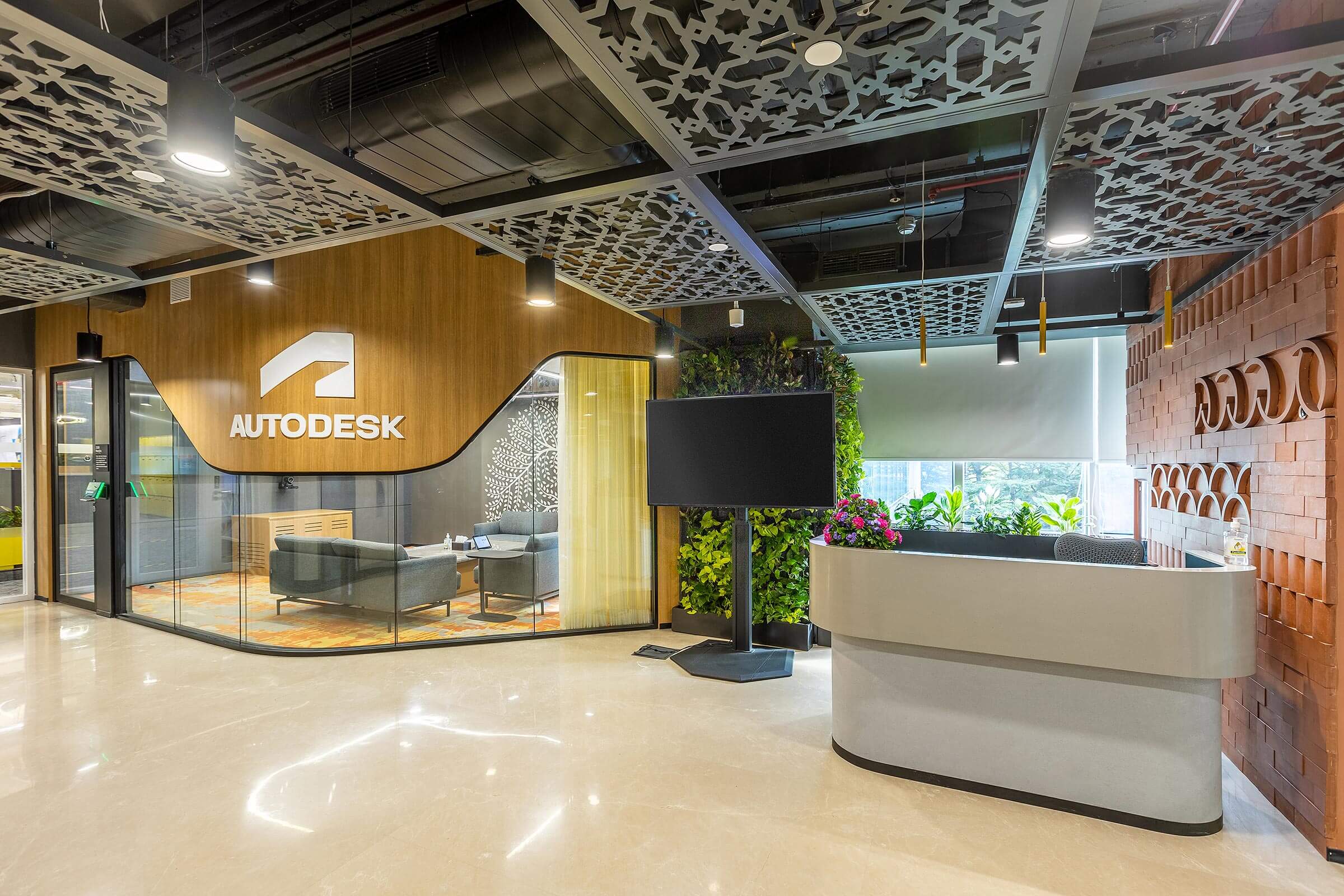 Reception desk with wood backdrop, logo signage, patterned ceiling panels, and indoor plants