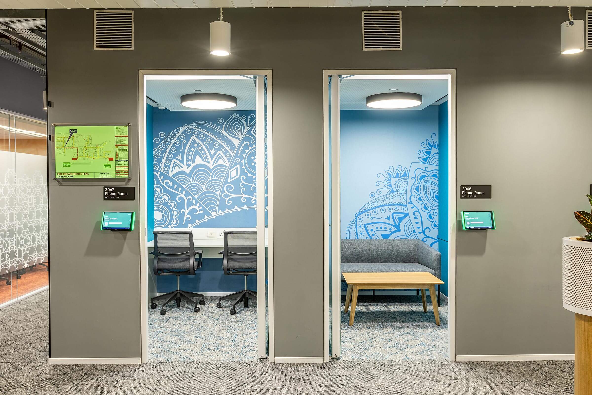 Corridor with enclosed phone rooms featuring blue graphic walls and digital booking panels