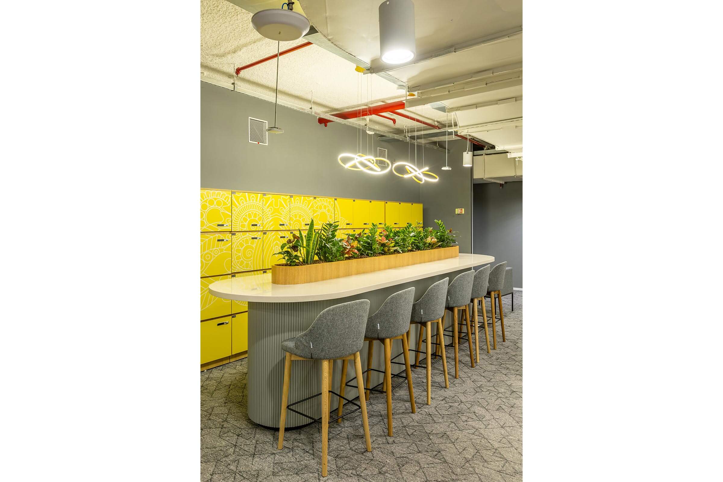 High collaboration counter with stools, planter centerpiece, yellow lockers, and pendant lighting