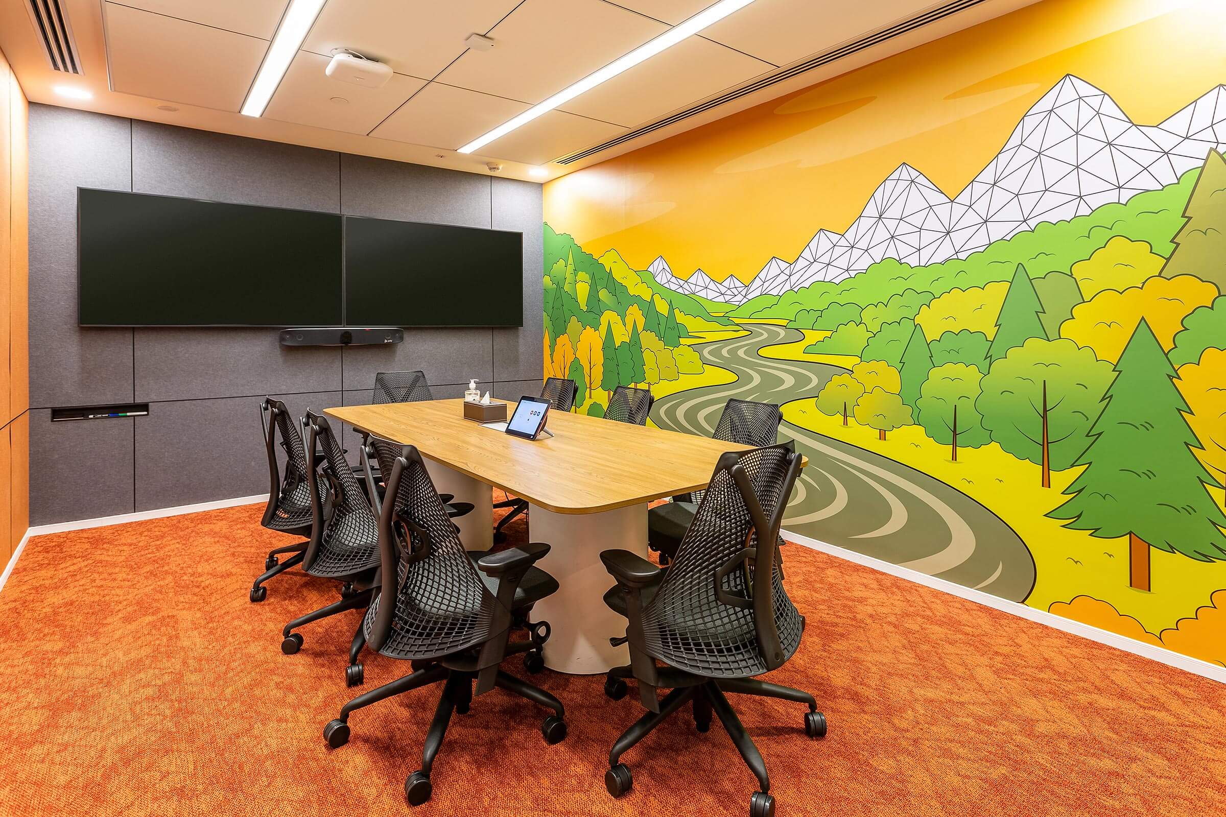 Conference room with long table, dual screens, and illustrated landscape wall graphic