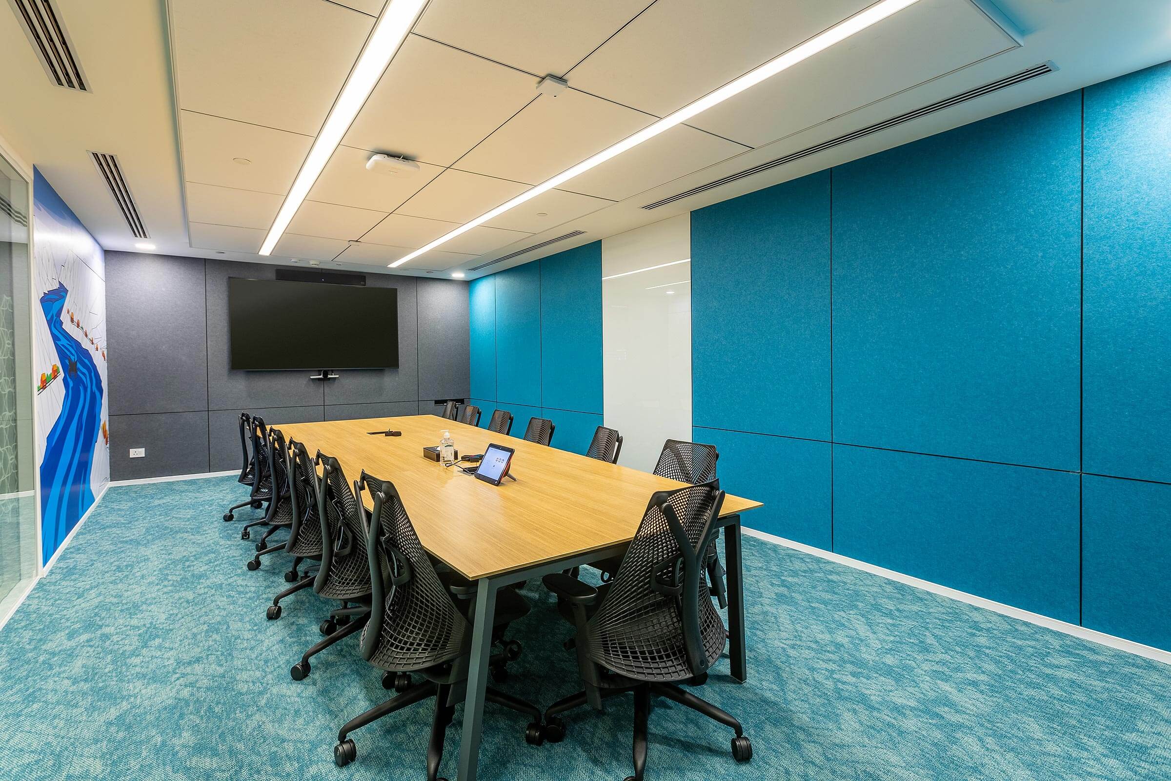 Boardroom with extended table, mesh task chairs, blue wall panels, and wall mounted display